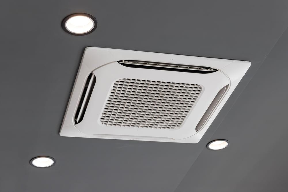 Ceiling cassette air conditioning unit fitted flush into a grey suspended ceiling beside recessed downlights