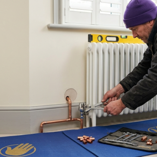 Engineer fitting a white column radiator and connecting copper pipework with a spirit level in place