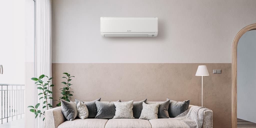 Wall-mounted split air conditioning unit installed above a sofa in a bright neutral living room